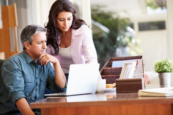 Worried man and woman stare at a laptop on a desk in a home office. They are worried about the impact of iBuyers, including Zillow, on their real estate appraisal business.